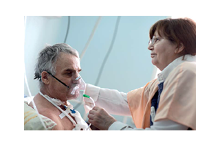[Image] Woman holding inhalator over man's mouth in hospital environment
