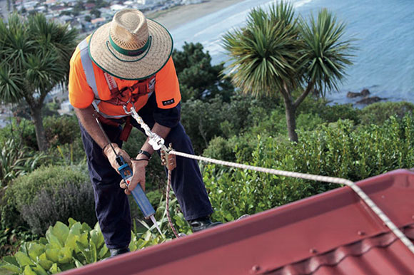 [image] Worker doing minor roof repairs wearing safety harness attached to stable positioning rope