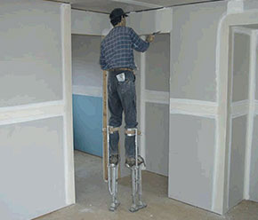 [image] A plasterer uses stilts to comfortably reach above door frames